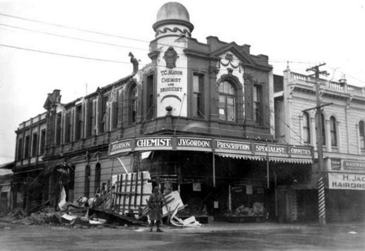 A soldier stands guard outside the heavily damaged chemist's shop operated by J.V. Gordon, on the corner of Queen and Bannister Streets. [Courtesy of Wairarapa Archive]